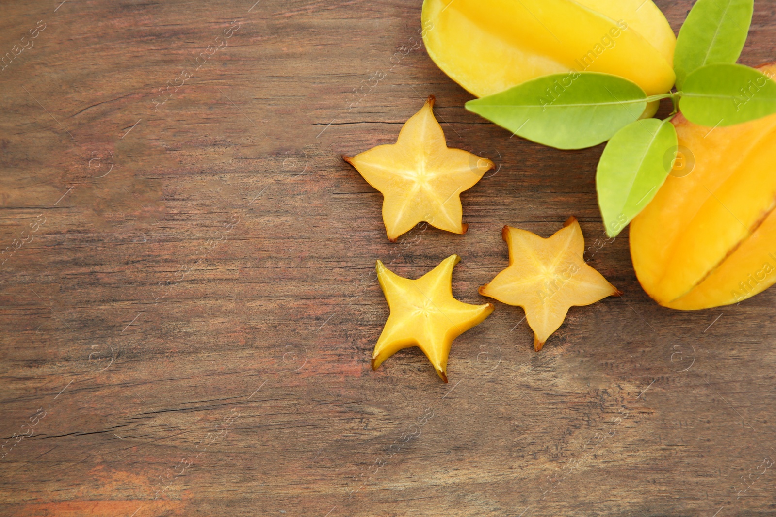 Photo of Cut and whole delicious ripe carambolas with leaves on wooden table, flat lay