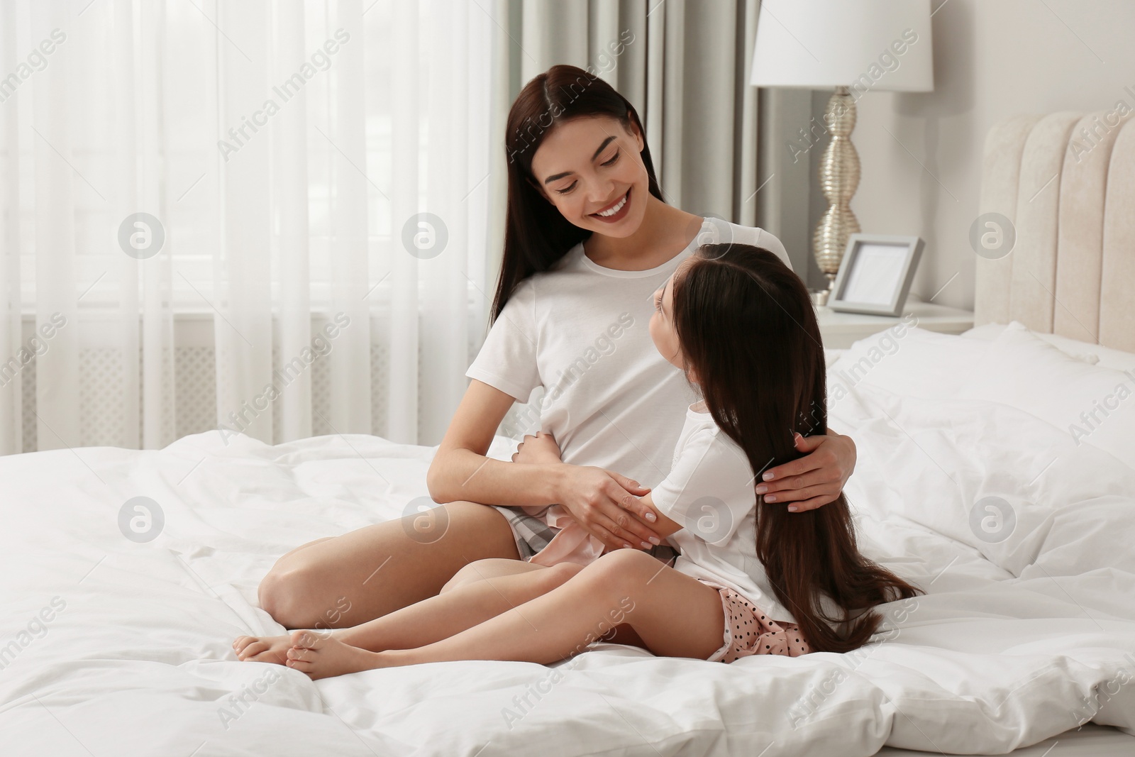 Photo of Young mother and her daughter on bed at home