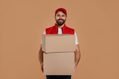 Photo of Happy young courier with parcels on light brown background