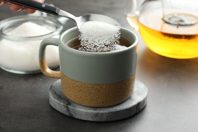 Woman adding sugar into aromatic tea at grey table, closeup