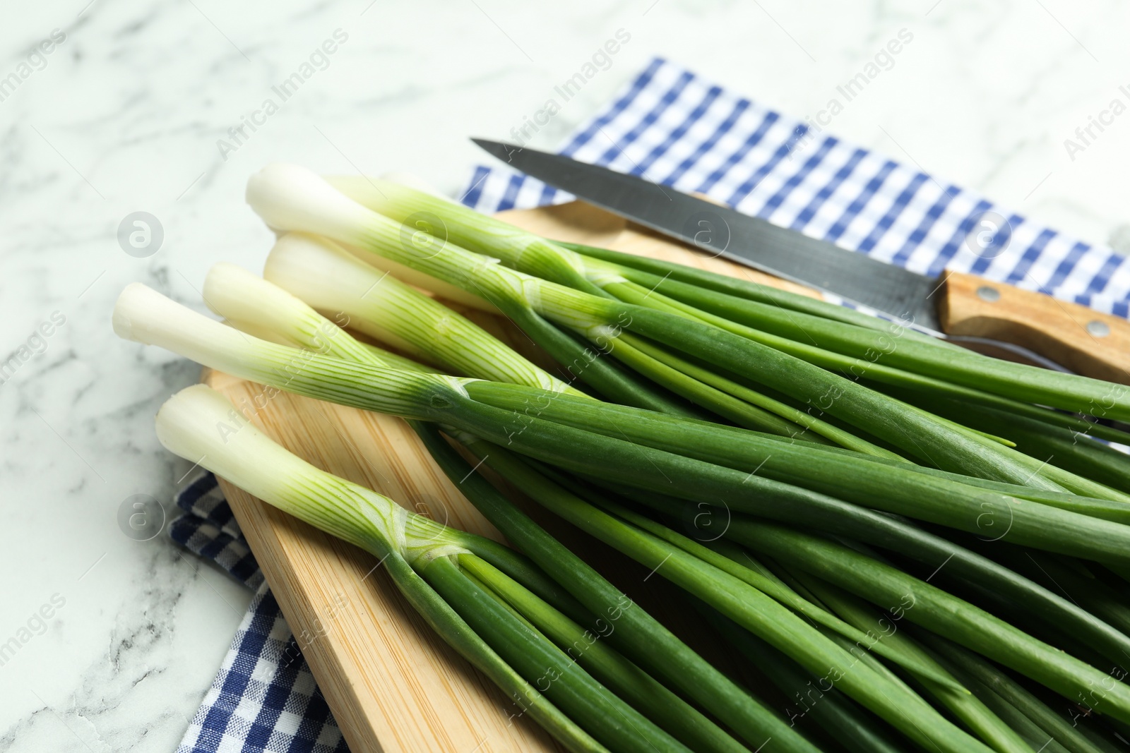 Photo of Fresh green spring onions on wooden board, closeup