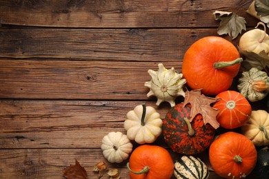 Different ripe pumpkins and dry leaves on wooden table, flat lay. Space for text