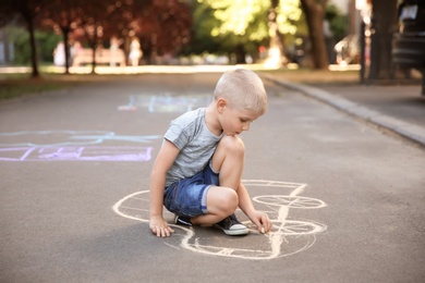 Photo of Little child drawing car with chalk on asphalt