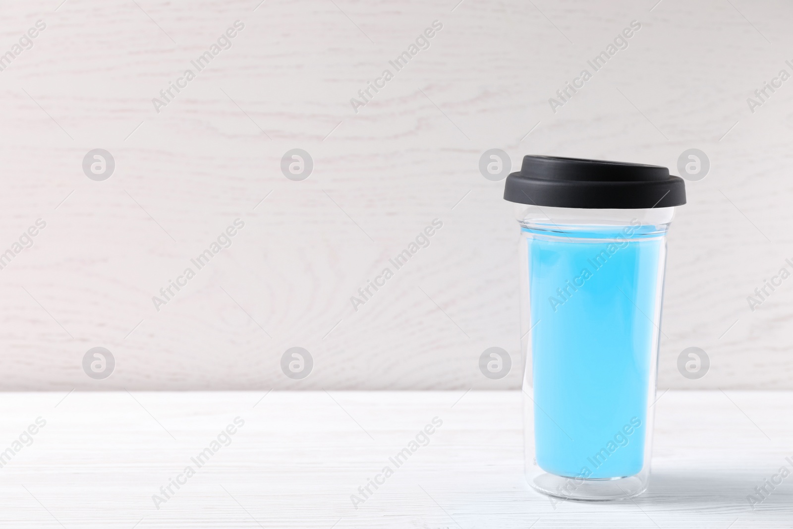 Photo of Bright light blue drink in glass with lid on white wooden table, space for text