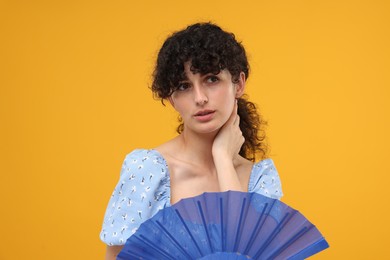 Photo of Woman with hand fan suffering from heat on orange background