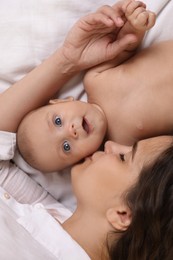 Young mother with her cute baby on bed, top view