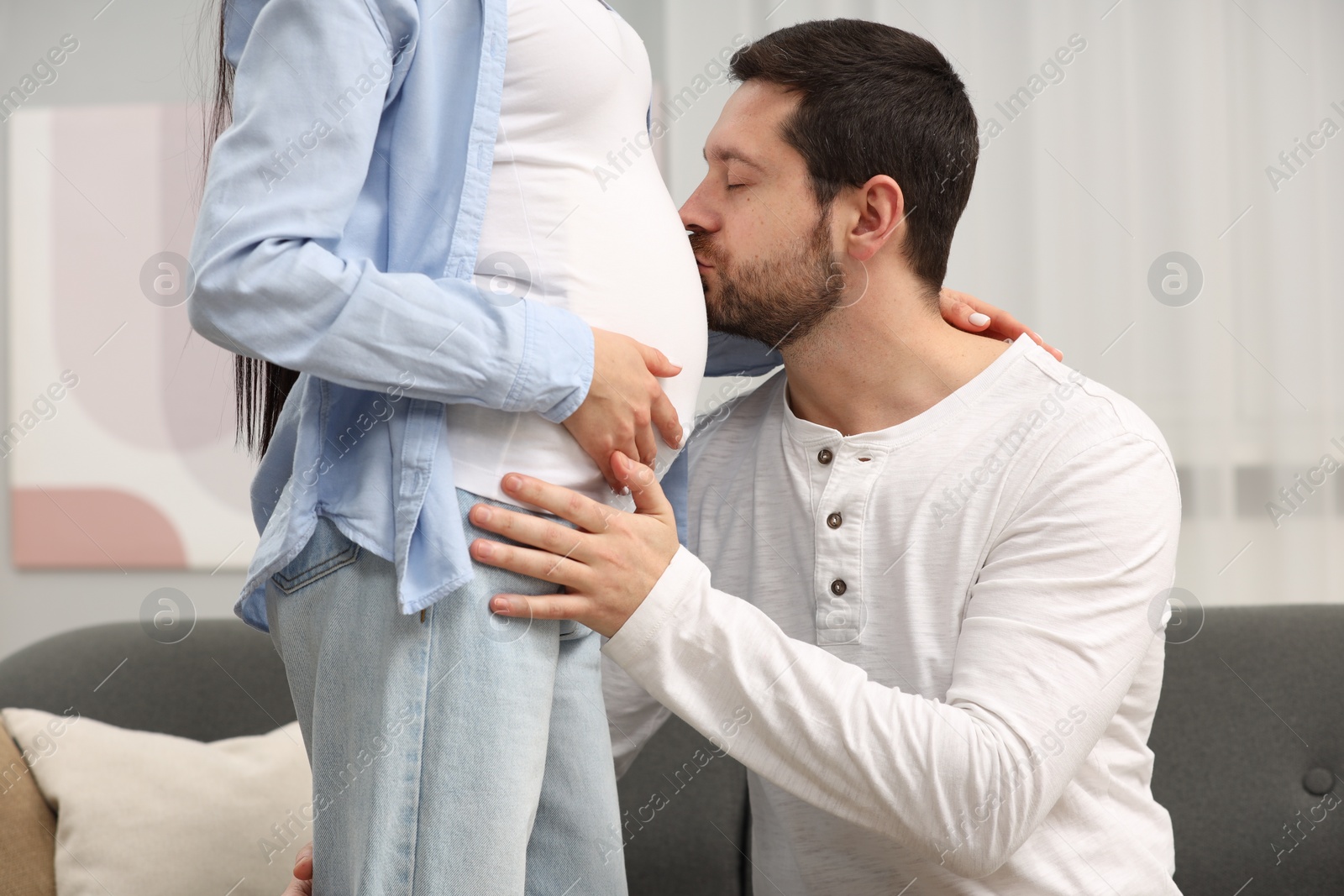 Photo of Happy husband kissing pregnant wife's belly at home