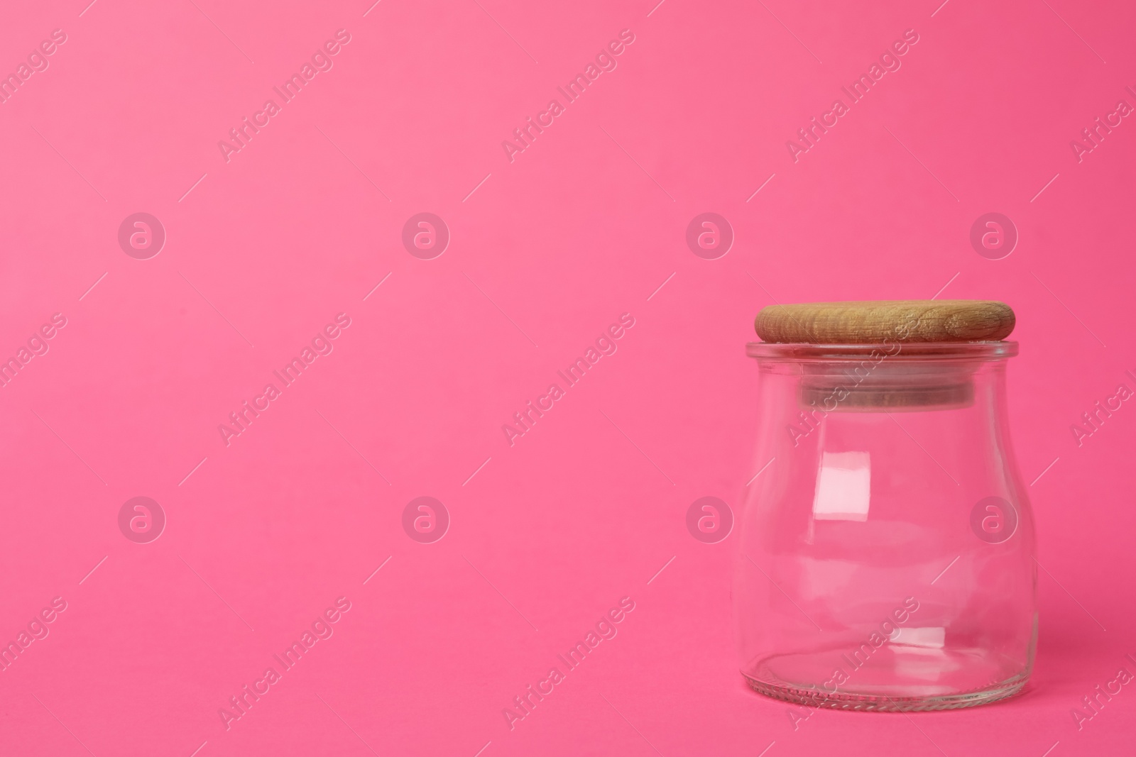 Photo of Closed empty glass jar on pink background, space for text