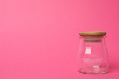Closed empty glass jar on pink background, space for text