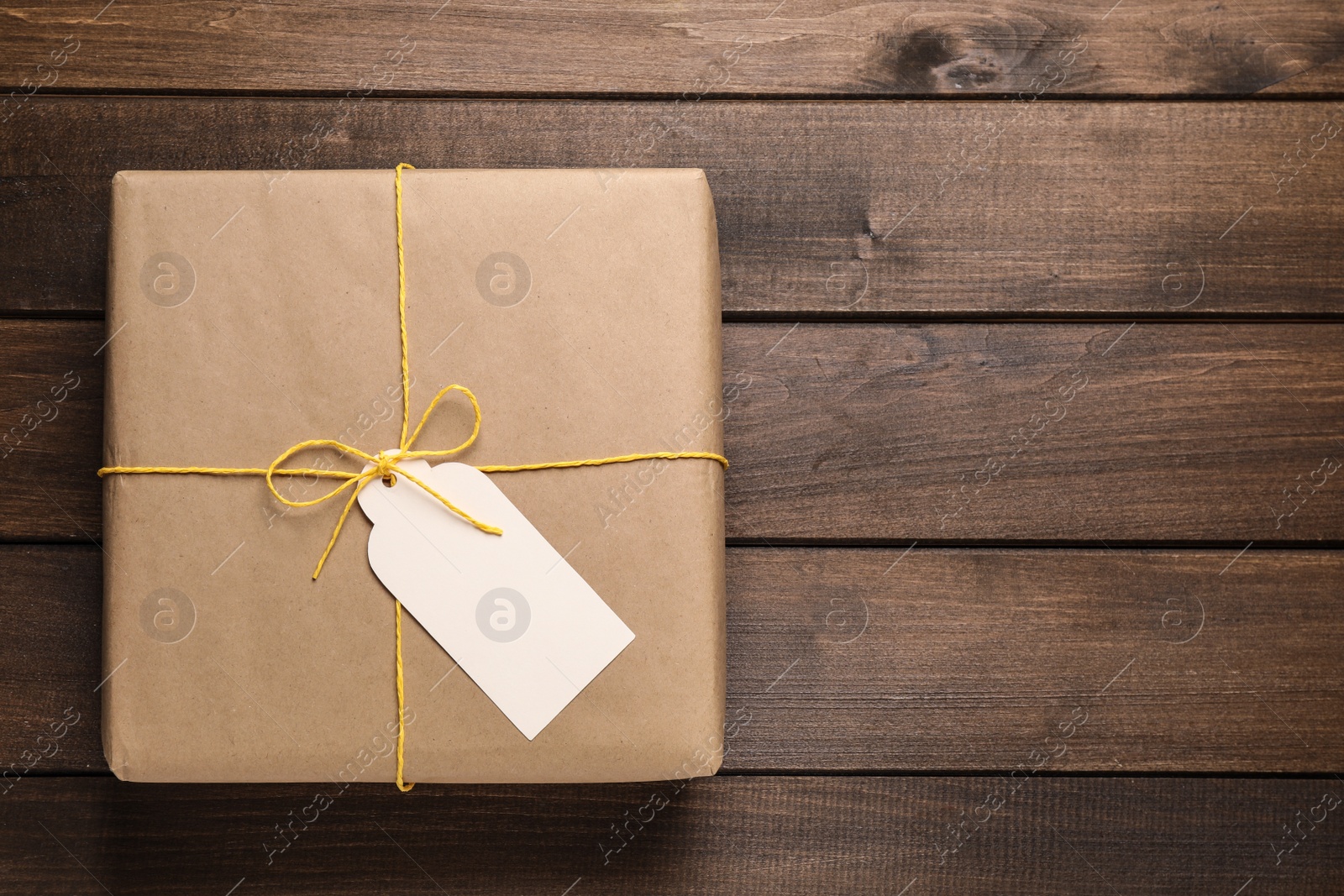 Photo of Parcel wrapped in kraft paper with tag on wooden table, top view. Space for text