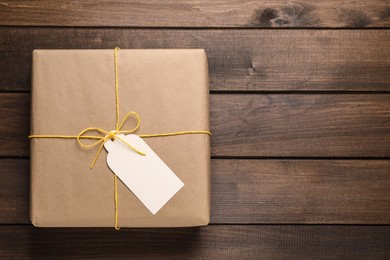 Parcel wrapped in kraft paper with tag on wooden table, top view. Space for text