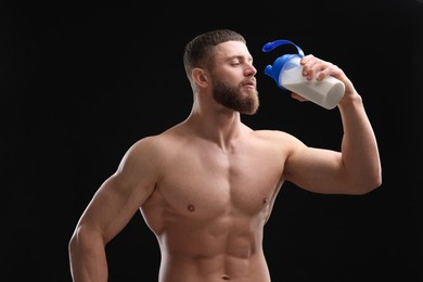 Young man with muscular body drinking protein shake on black background