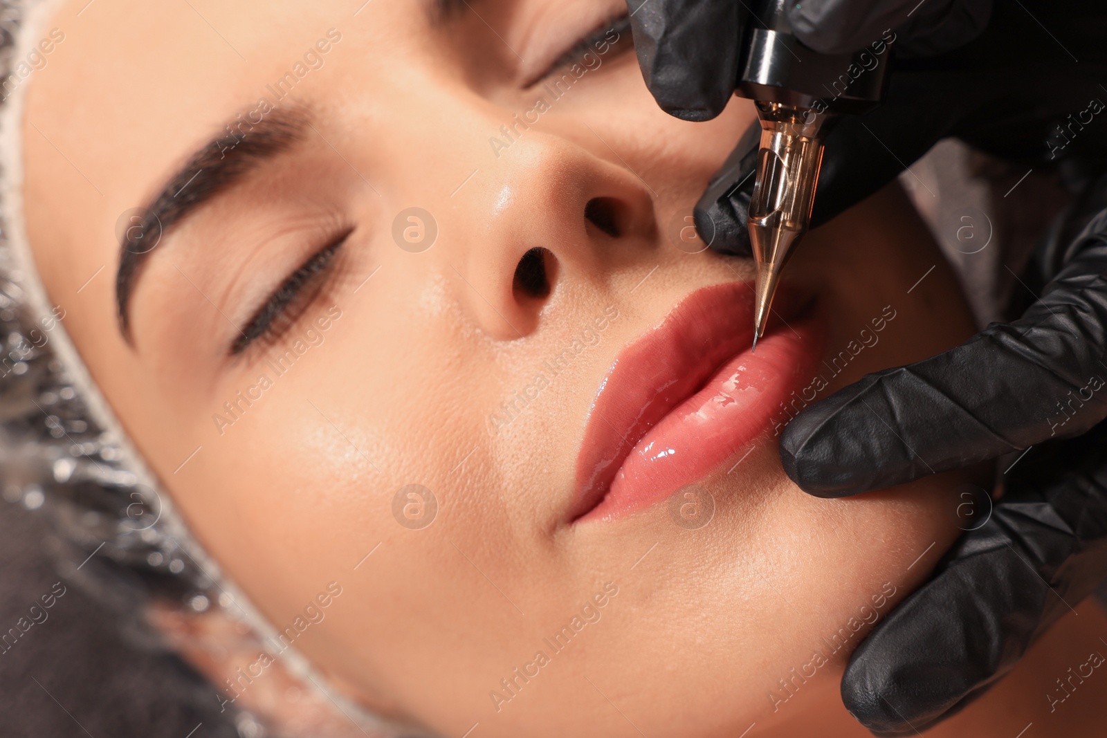 Photo of Young woman undergoing procedure of permanent lip makeup in tattoo salon, closeup