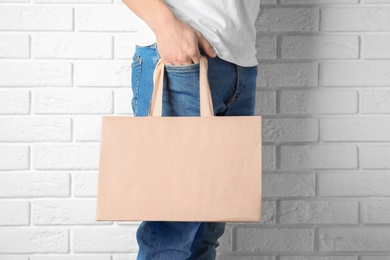Photo of Man holding mock-up of paper shopping bag against wall
