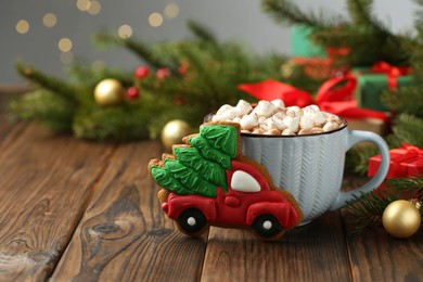 Photo of Tasty Christmas cookie in shape of car with fir tree, cocoa with marshmallows and festive decor on wooden table, closeup. Space for text
