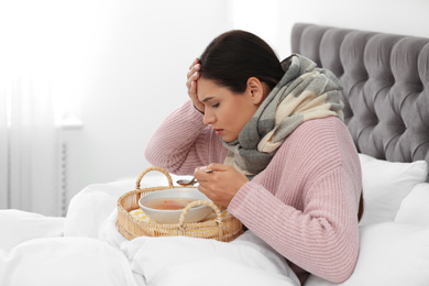 Photo of Sick young woman eating soup to cure flu in bed at home