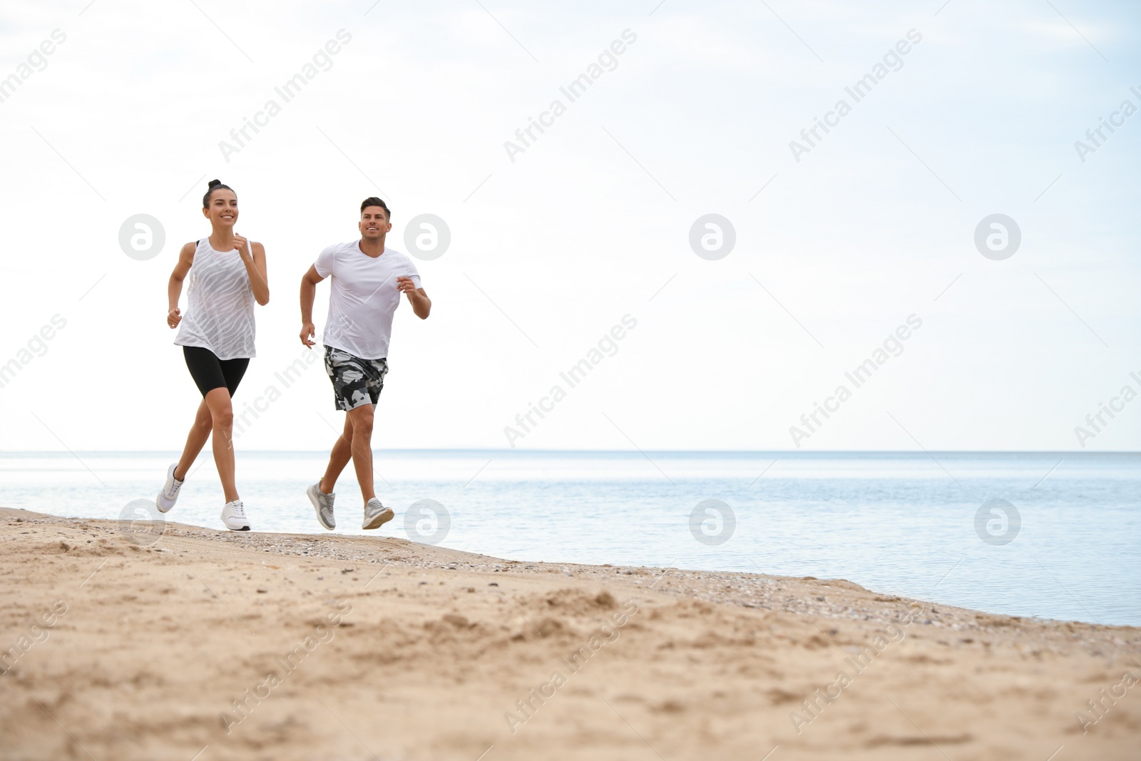 Photo of Couple running together on beach, space for text. Body training