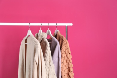 Photo of Collection of warm sweaters hanging on rack against color background. Space for text