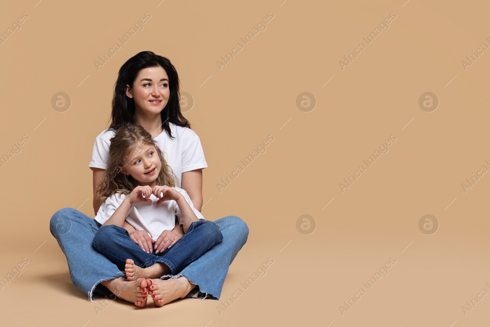 Photo of Beautiful mother with little daughter sitting on beige background. Space for text