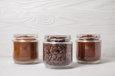 Jars with instant, ground coffee and roasted beans on white wooden table