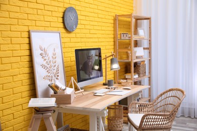 Stylish home office interior with comfortable workplace near yellow brick wall