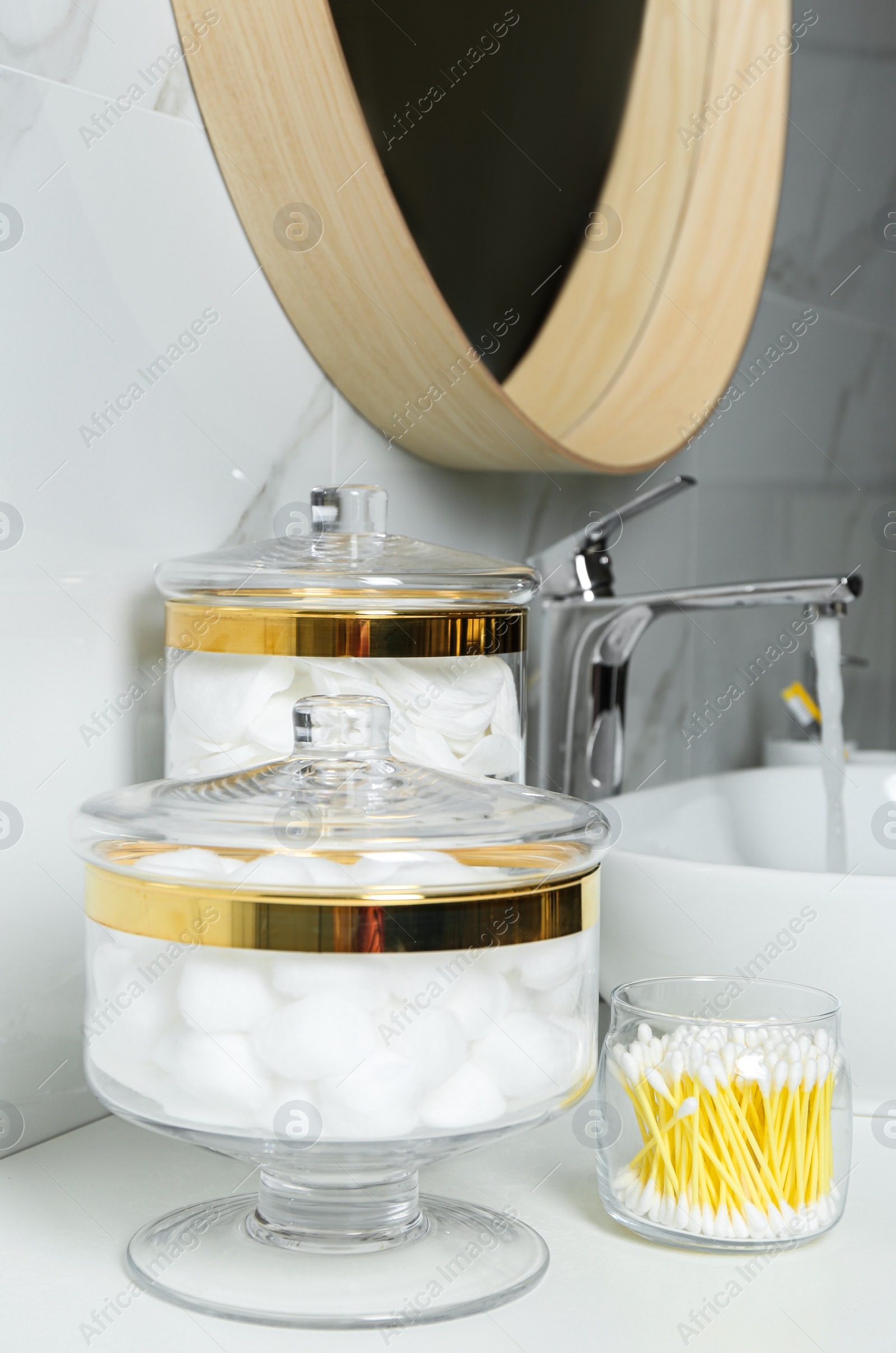 Photo of Jars with cotton balls, swabs and pads on white countertop in bathroom