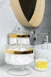 Photo of Jars with cotton balls, swabs and pads on white countertop in bathroom