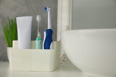 Photo of Electric toothbrushes and tube of paste near vessel sink on countertop in bathroom, closeup