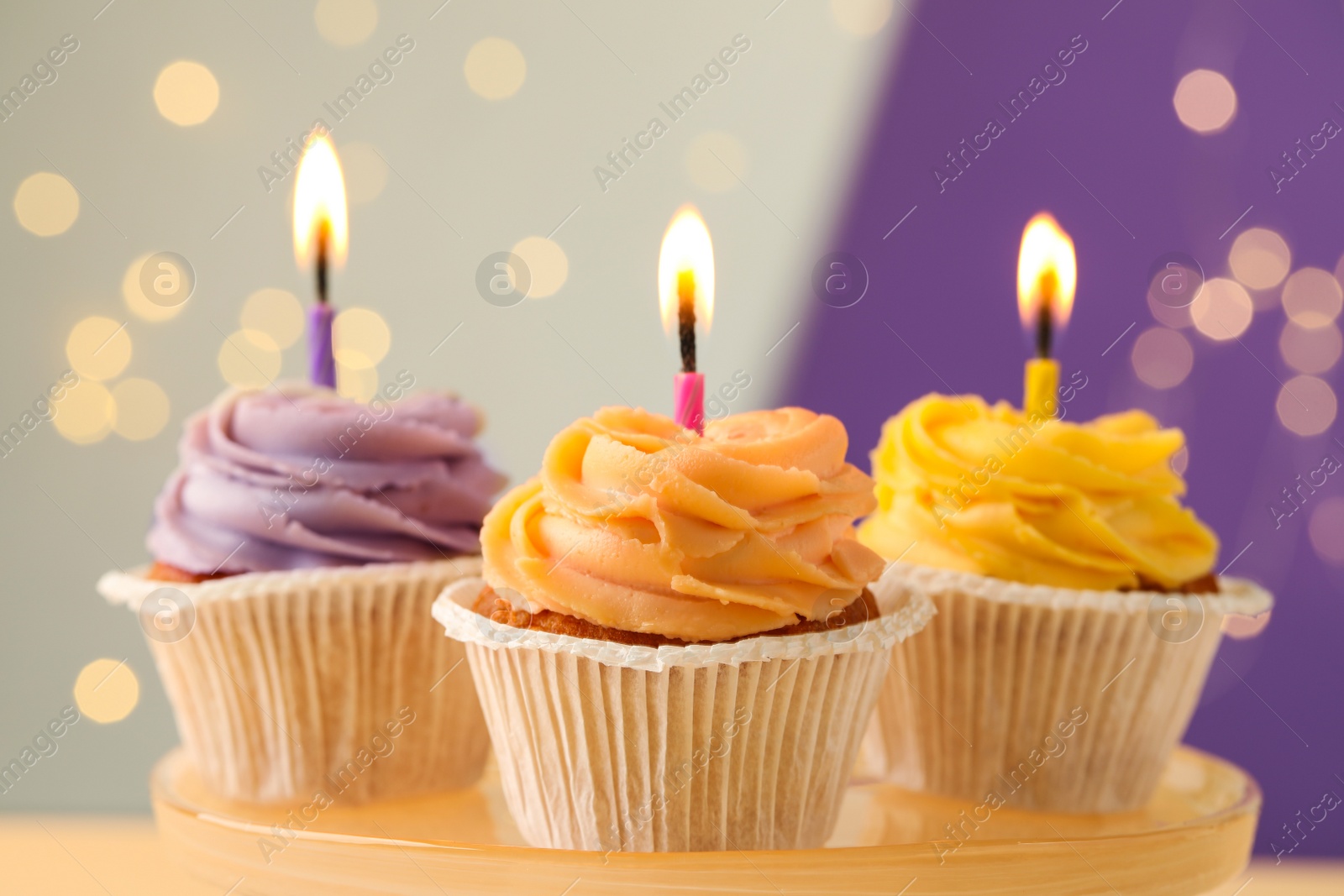 Photo of Tasty birthday cupcakes with candles on stand against blurred lights, closeup