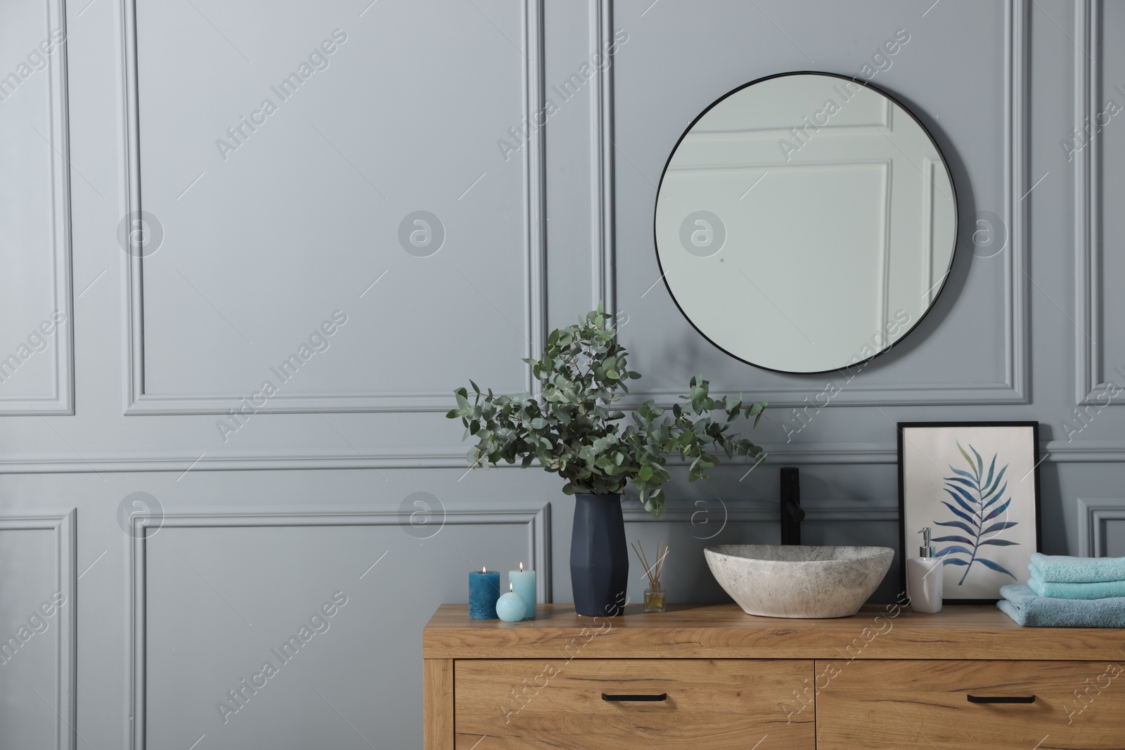 Photo of Folded towels, burning candles and eucalyptus branches near vessel sink on bathroom vanity. Interior design