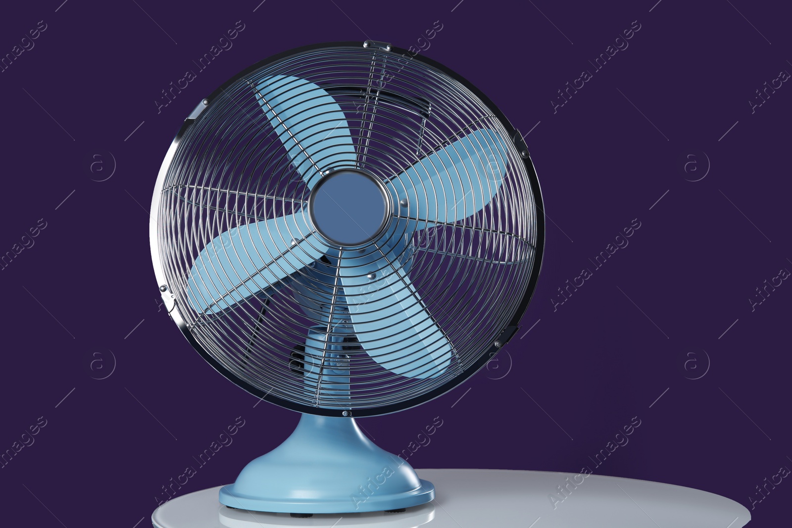 Photo of Modern electric fan on white table against violet background