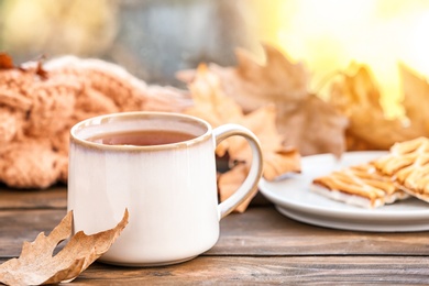 Photo of Cup of hot cozy drink and autumn leaf on windowsill. Space for text