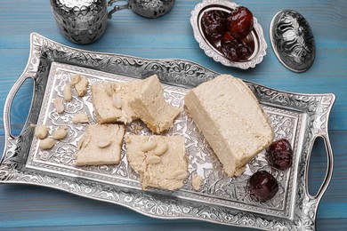 Pieces of tasty halva, dates and peanuts served in vintage tea set on light blue wooden table, above view