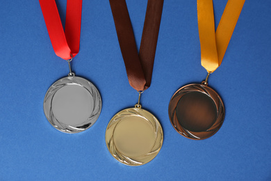 Gold, silver and bronze medals on blue background, flat lay. Space for design