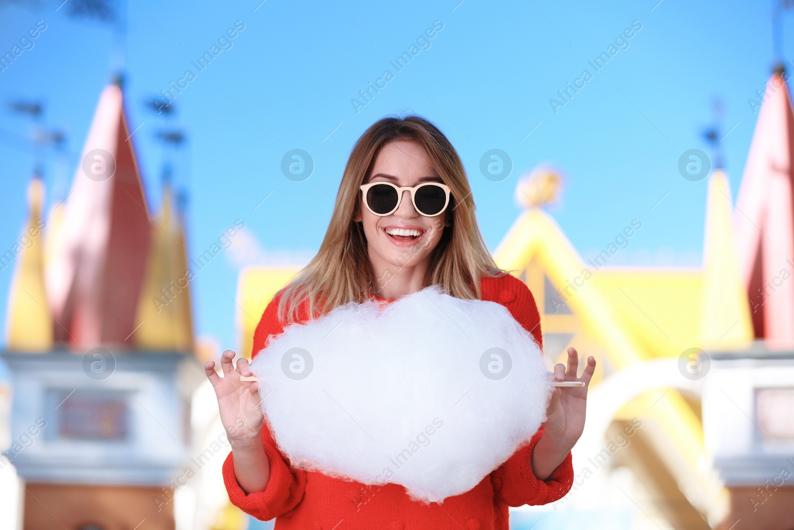 Photo of Young cheerful woman having fun with  cotton candy in amusement park