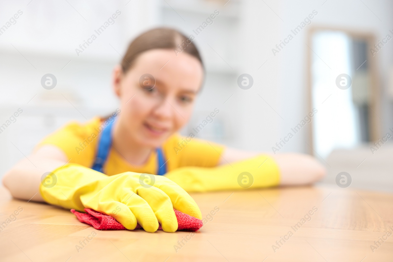 Photo of Woman cleaning wooden table with rag indoors, selective focus