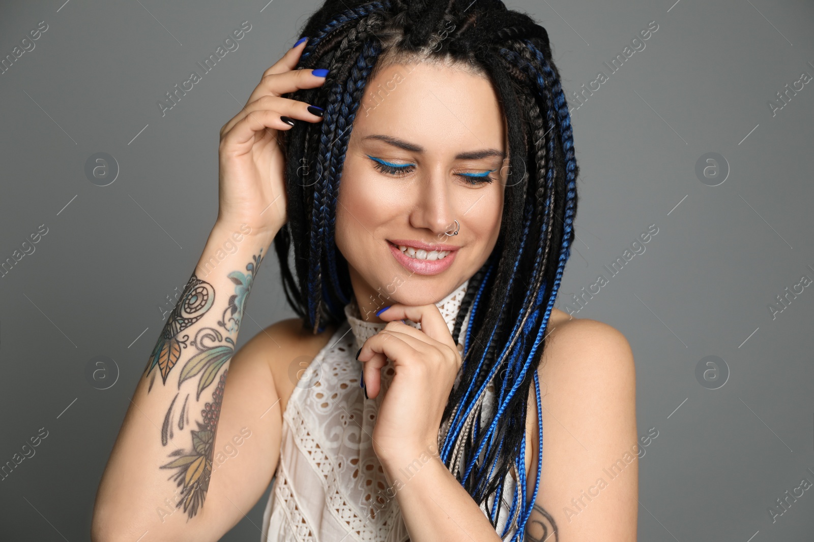 Photo of Beautiful young woman with nose piercing and dreadlocks on grey background