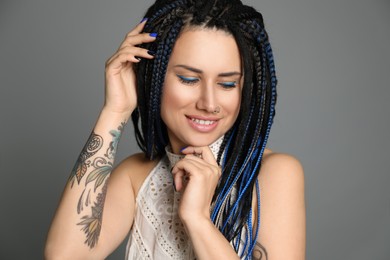 Beautiful young woman with nose piercing and dreadlocks on grey background