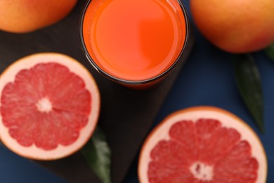 Photo of Tasty grapefruit juice in glass and fresh fruits on blue table, flat lay