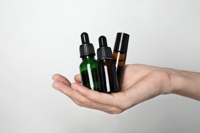 Photo of Woman holding bottles of essential oil on light background, closeup
