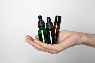 Woman holding bottles of essential oil on light background, closeup