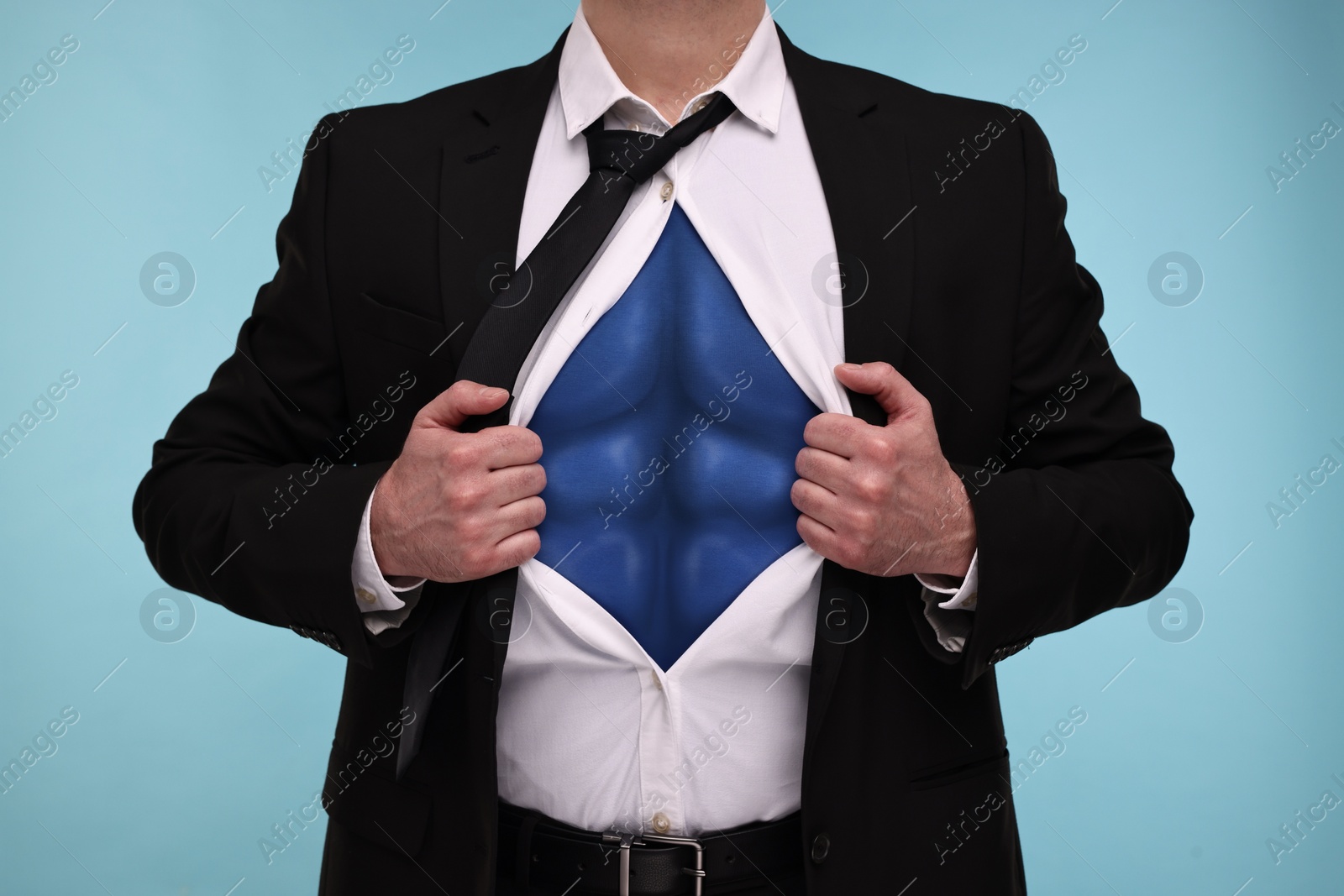 Image of Businessman wearing superhero costume under suit on light blue background, closeup