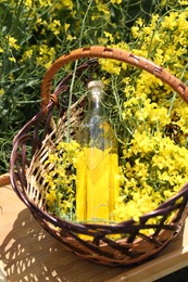 Wicker basket with rapeseed oil and flowers outdoors, closeup