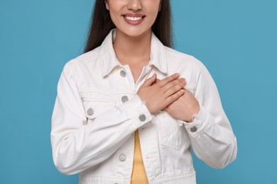 Thank you gesture. Grateful woman with hands on chest against light blue background, closeup