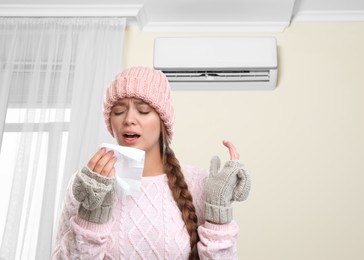 Woman suffering from cold in room with air conditioner on white wall