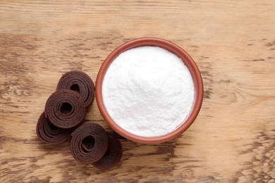 Photo of Bowl of fructose powder and fruit leather rolls on wooden table, flat lay