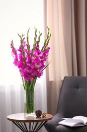 Vase with beautiful pink gladiolus flowers on wooden table in room, space for text