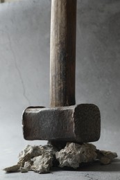 Photo of One sledgehammer and pieces of broken stones on grey background, closeup