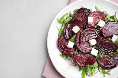 Roasted beetroot slices with feta cheese and arugula on light grey table, top view. Space for text