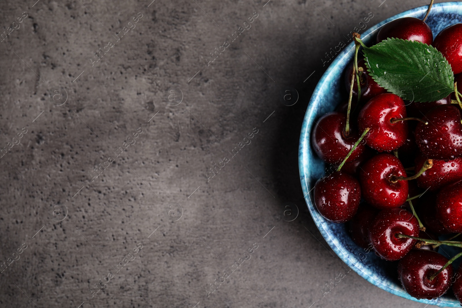 Photo of Bowl with delicious sweet cherries on grey table, top view. Space for text